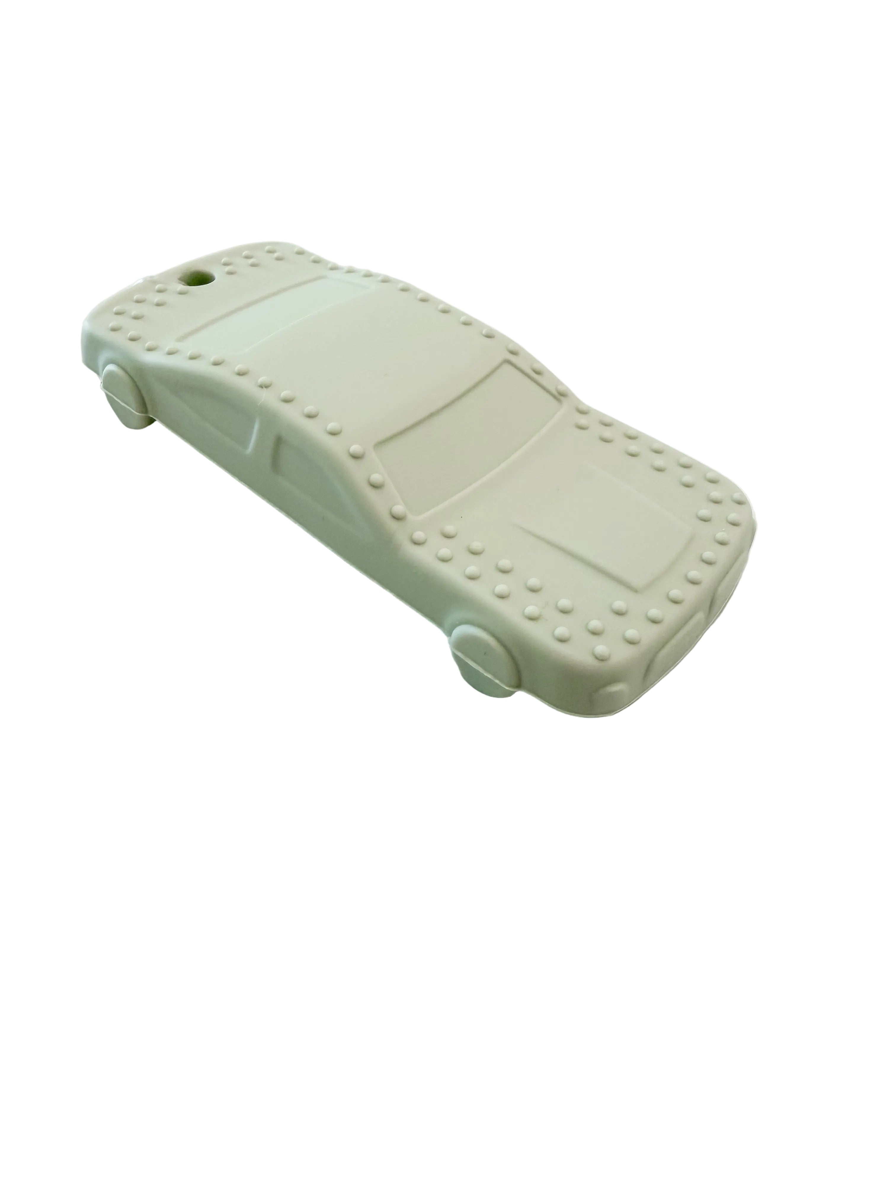 A pale mint green car-shaped silicone teether with raised stud details around the edges, resting on a white marble-patterned surface.