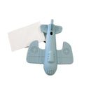 A light blue airplane-shaped silicone lip balm tube lying on a white marble surface next to a blank white card.