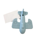 A light blue airplane-shaped silicone lip balm tube lying on a white marble surface next to a blank white card.