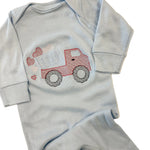 Light blue baby onesie with red truck design on a beige surface