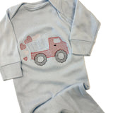 Light blue baby onesie with red truck design on a beige surface