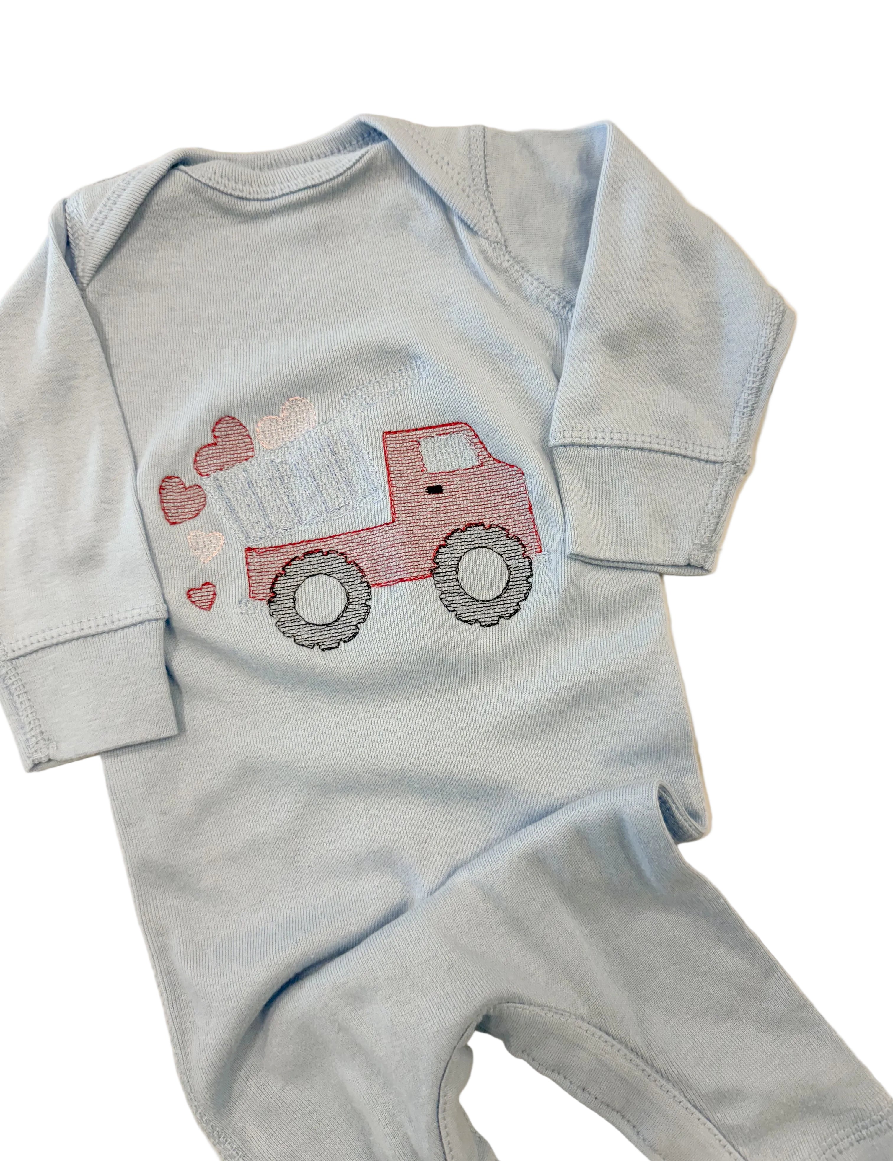 Light blue baby onesie with red truck design on a beige surface
