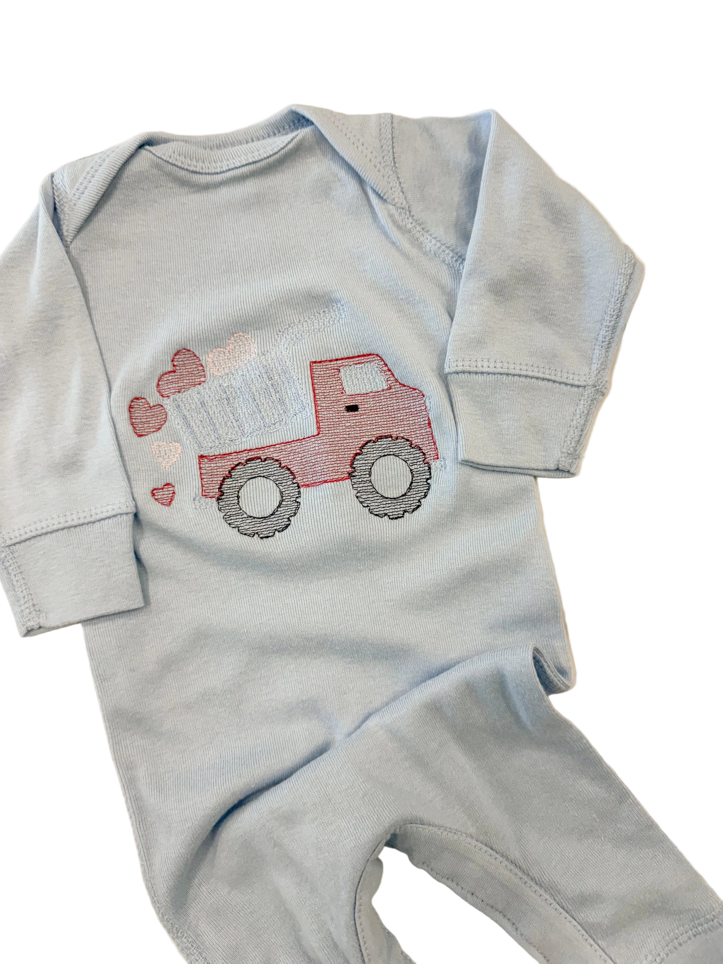 Light blue baby onesie with red truck design on a beige surface