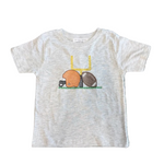 A light heather gray baby t-shirt laid flat on a dark patterned rug. The shirt features a graphic of a yellow chair with a brown football and an orange duck wearing a football helmet.