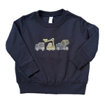 A navy blue long-sleeve sweatshirt for toddlers, featuring a graphic of three construction vehicles (a dump truck, a crane, and a cement mixer) on the chest. The sweatshirt is laid flat on a blue and beige patterned rug.