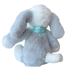 Gray plush bunny with a green bow tie on a white surface in a store setting.