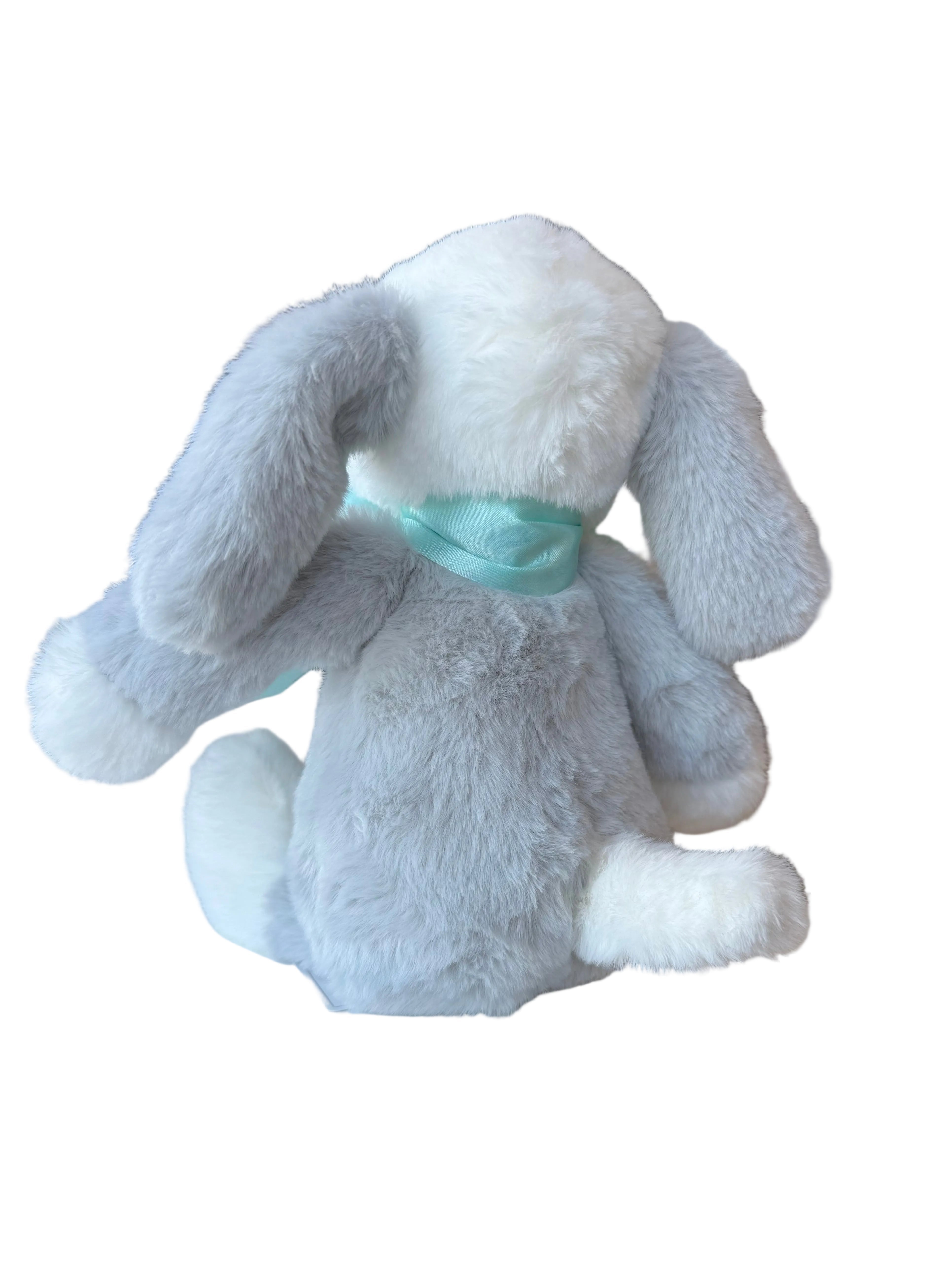 Gray plush bunny with a green bow tie on a white surface in a store setting.