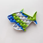Fish-shaped pop-it toy with blue, green, and white bubbles on a light gray background