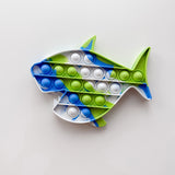 Fish-shaped pop-it toy with blue, green, and white bubbles on a light gray background