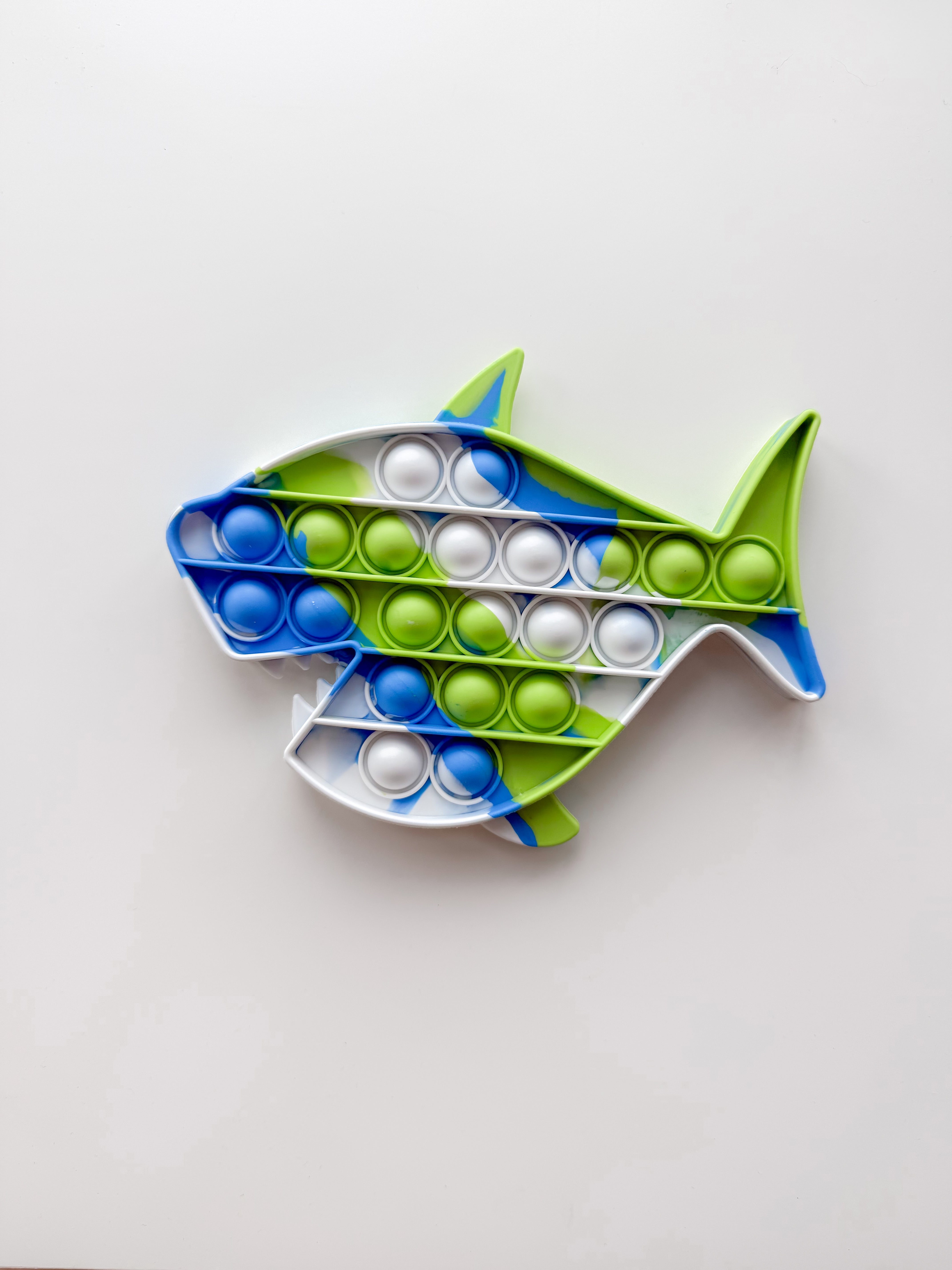 Fish-shaped pop-it toy with blue, green, and white bubbles on a light gray background