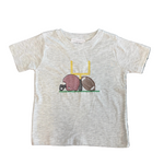 A toddler's short-sleeve heather gray t-shirt featuring a football-themed graphic with a pink helmet, brown football, and yellow goalpost, laid flat on a patterned gray rug.