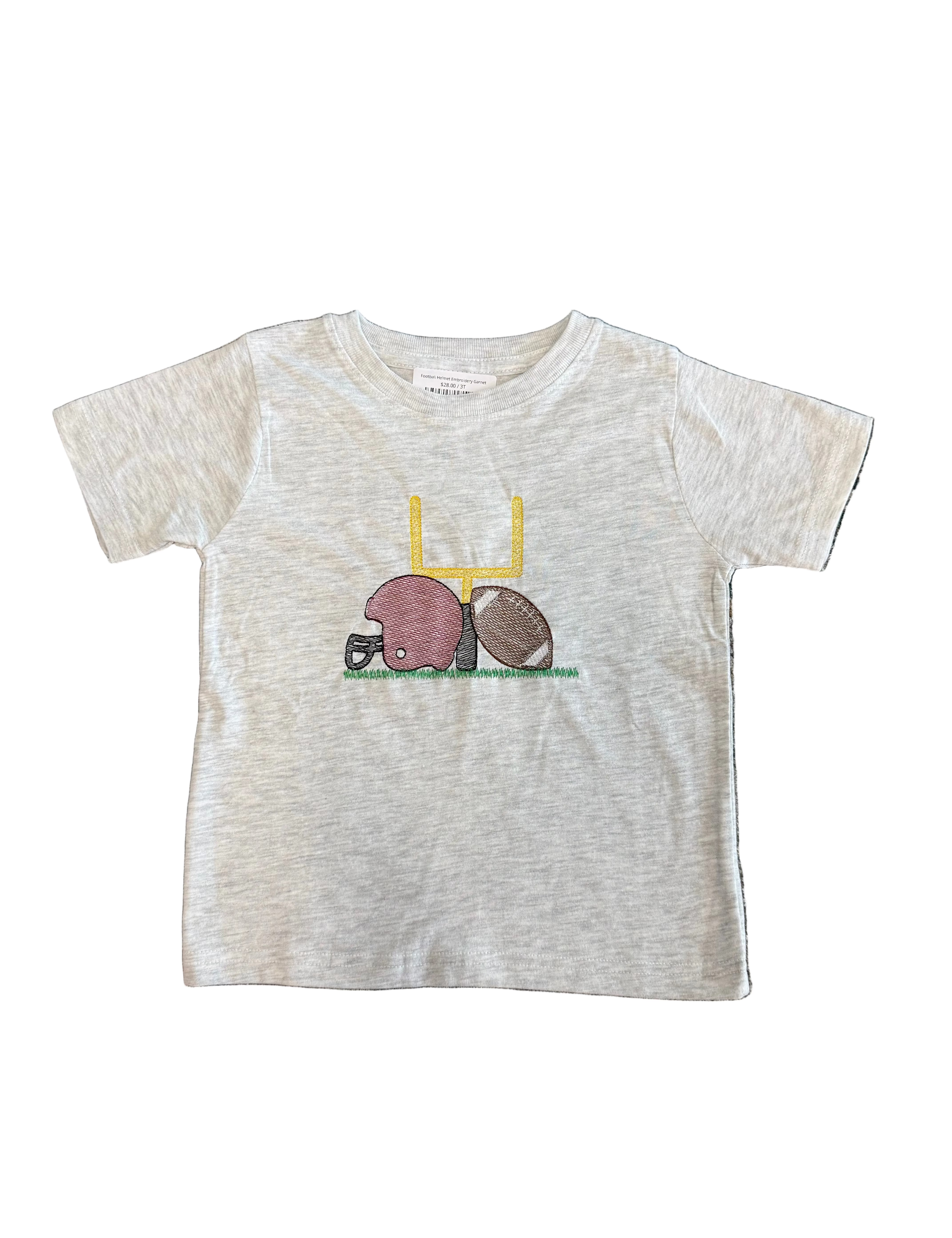 A toddler's short-sleeve heather gray t-shirt featuring a football-themed graphic with a pink helmet, brown football, and yellow goalpost, laid flat on a patterned gray rug.