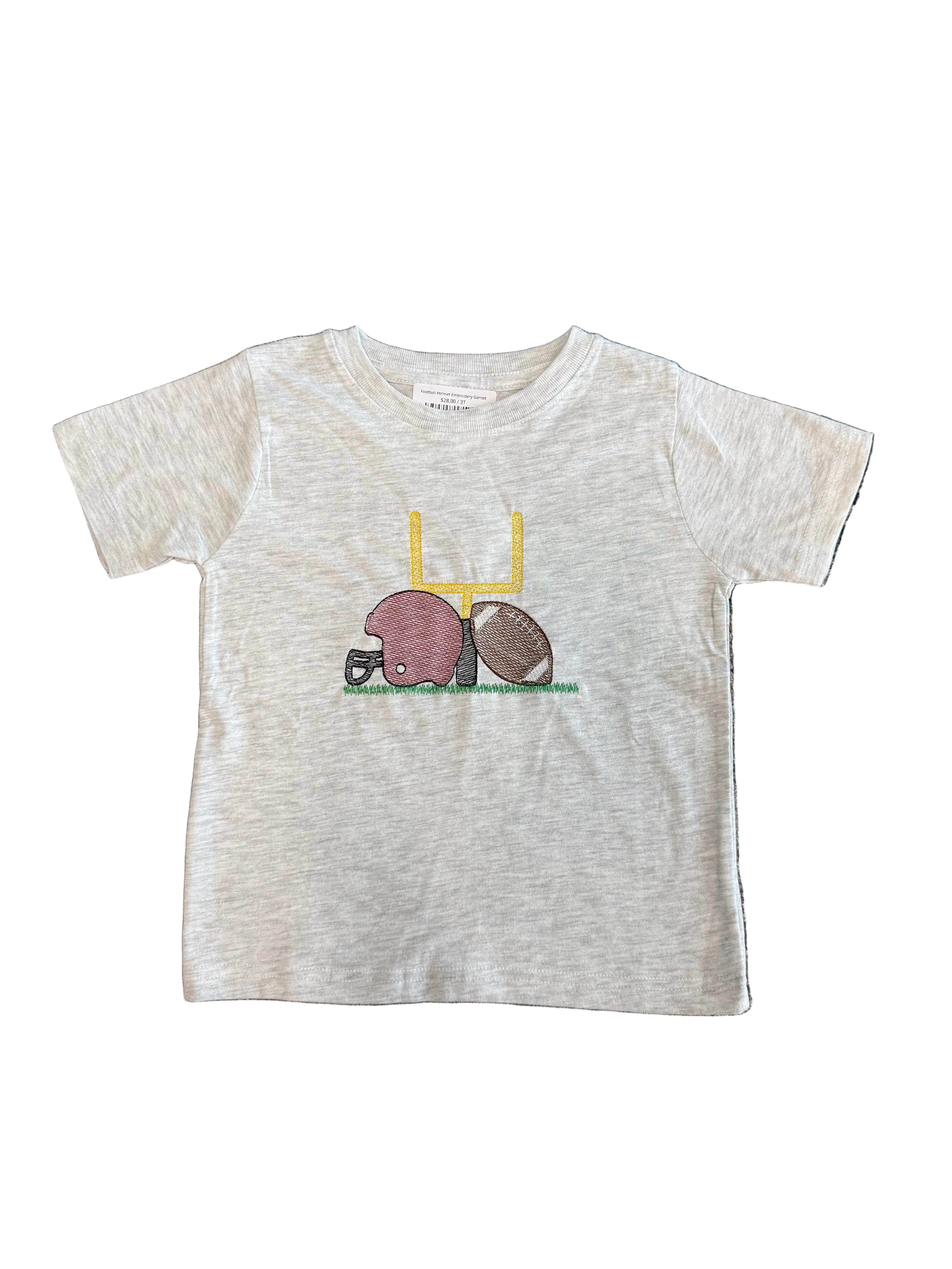 A toddler's short-sleeve heather gray t-shirt featuring a football-themed graphic with a pink helmet, brown football, and yellow goalpost, laid flat on a patterned gray rug.