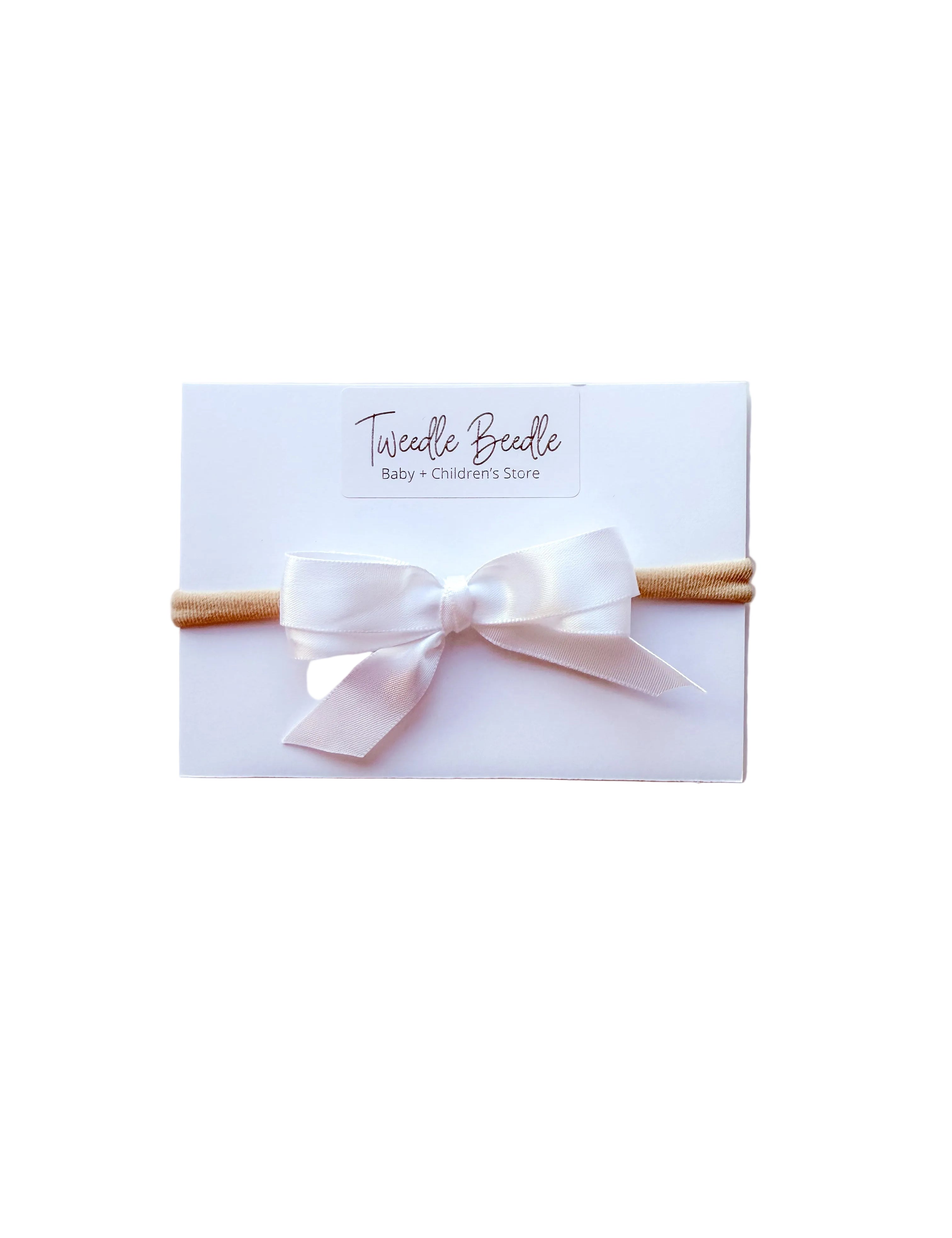 Baby headband with a white bow on a white card, branded 'Twiddle Beeddle'.