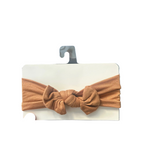 Brown knotted headband on a card held by a hand with a store interior in the background