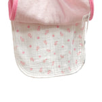 Baby bib with pink trim held up against a store display with various baby items.