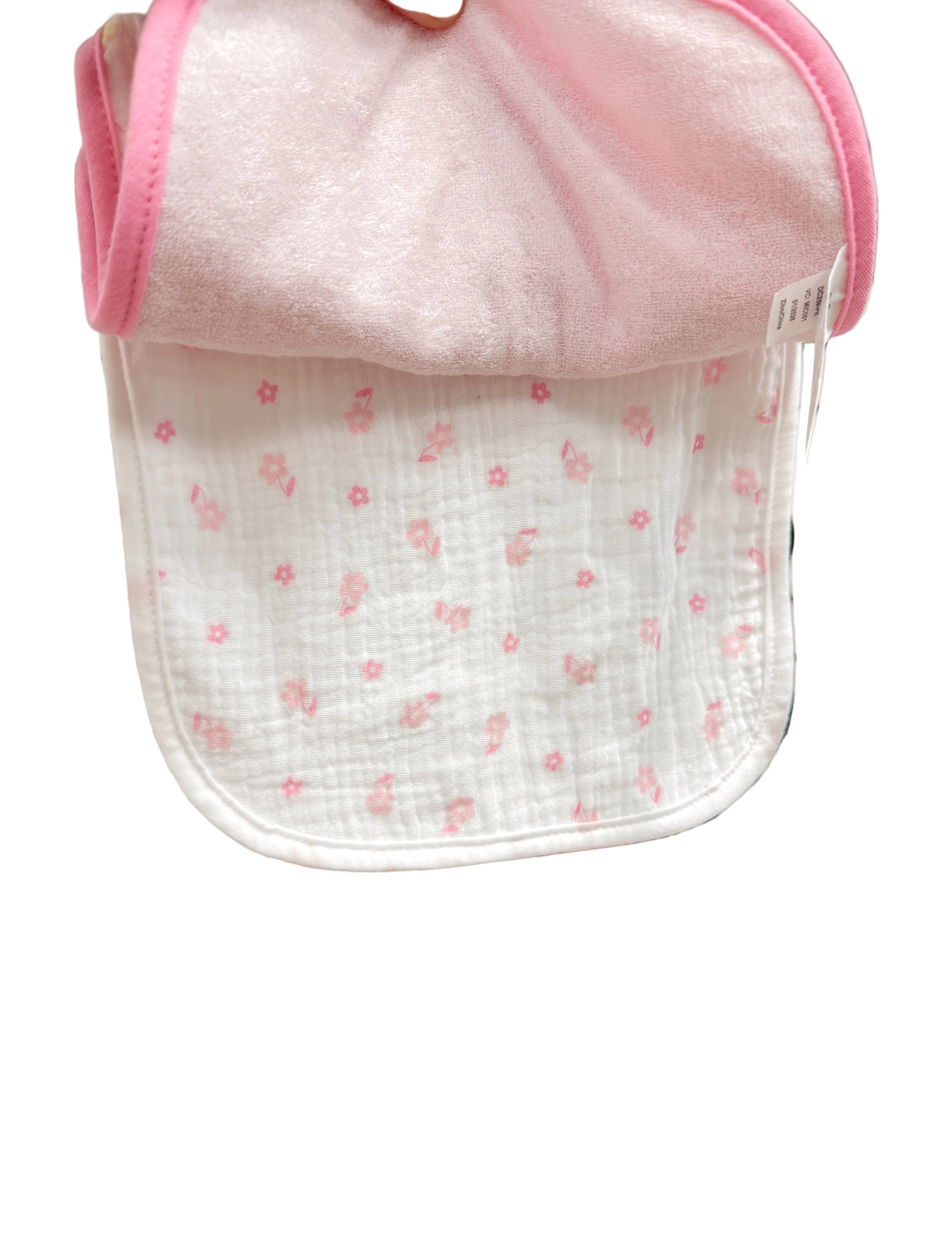 Baby bib with pink trim held up against a store display with various baby items.