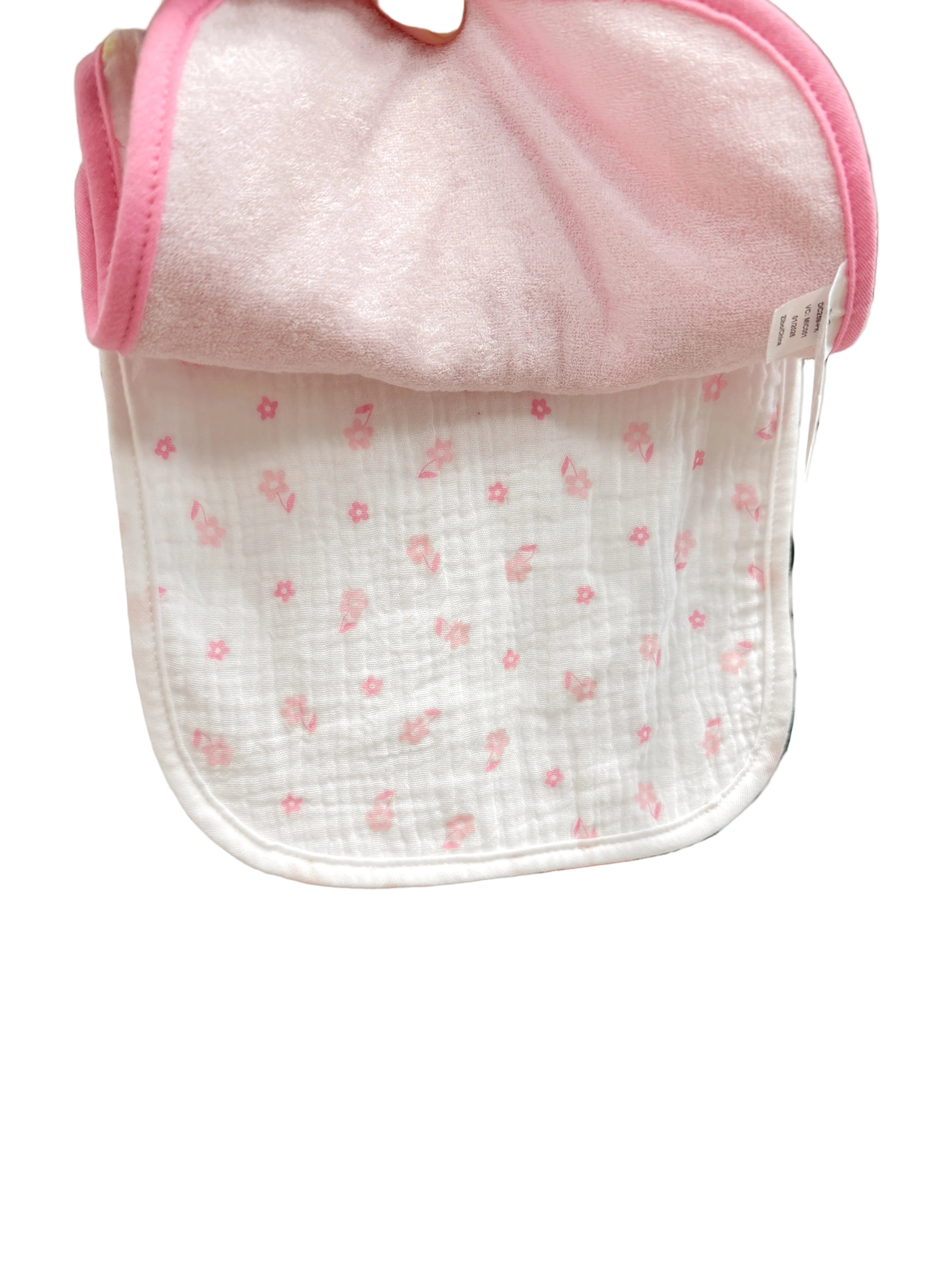 Baby bib with pink trim held up against a store display with various baby items.