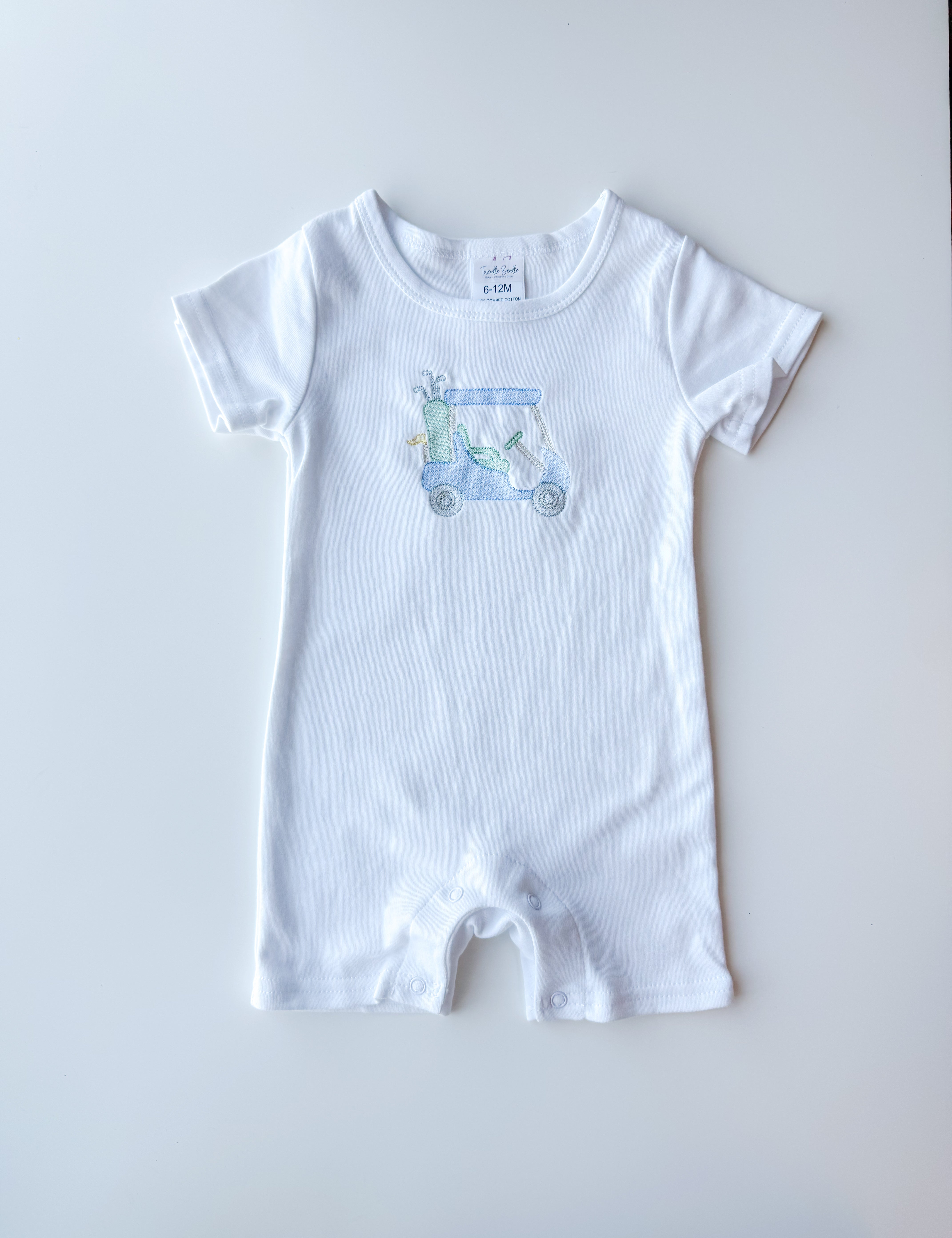 A white short-sleeve baby romper with a small light blue and green golf cart graphic on the chest, laid flat on a light gray background.