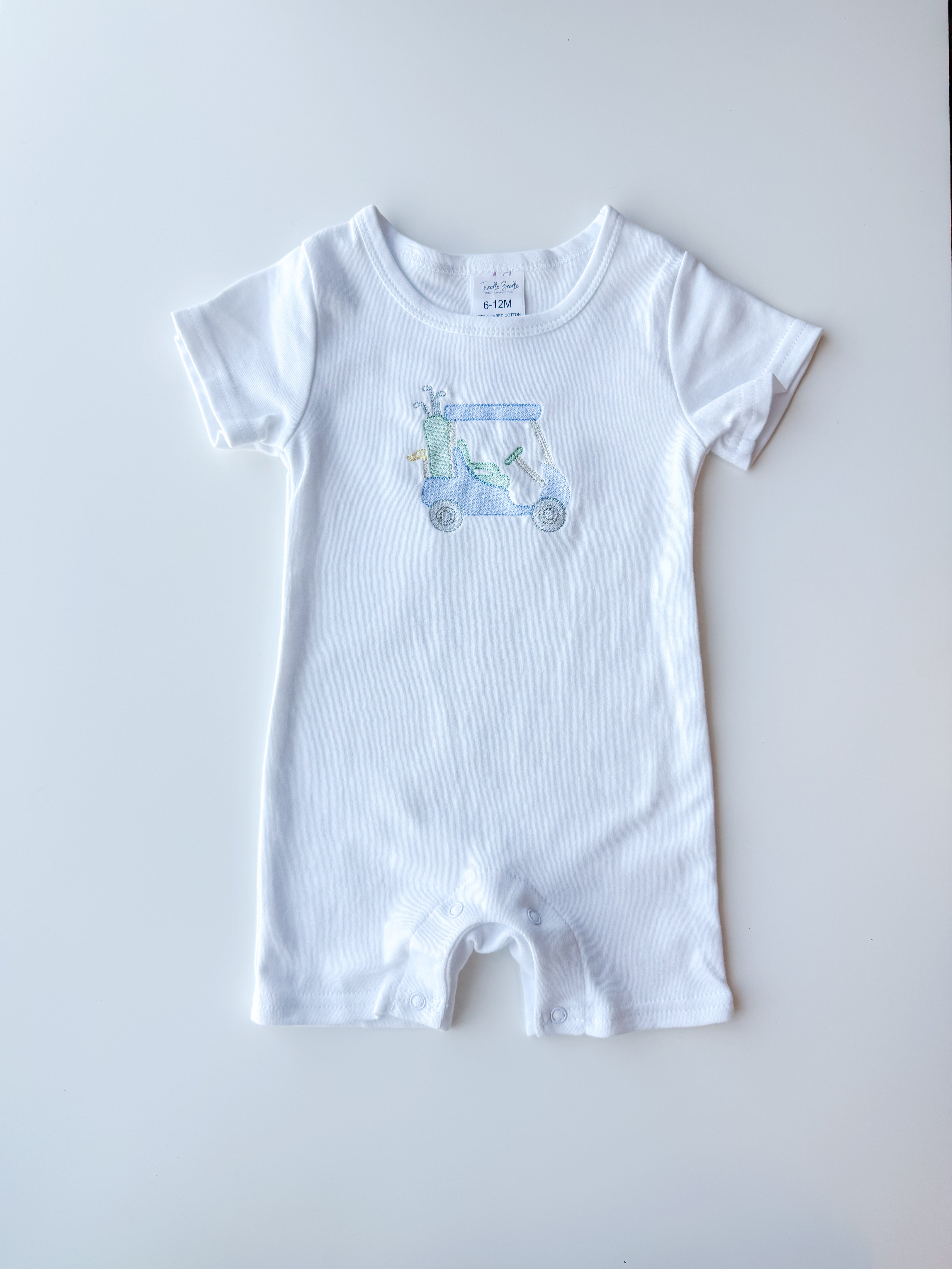 A white short-sleeve baby romper with a small light blue and green golf cart graphic on the chest, laid flat on a light gray background.