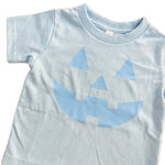 Light blue t-shirt with a jack-o'-lantern face design on a wooden surface