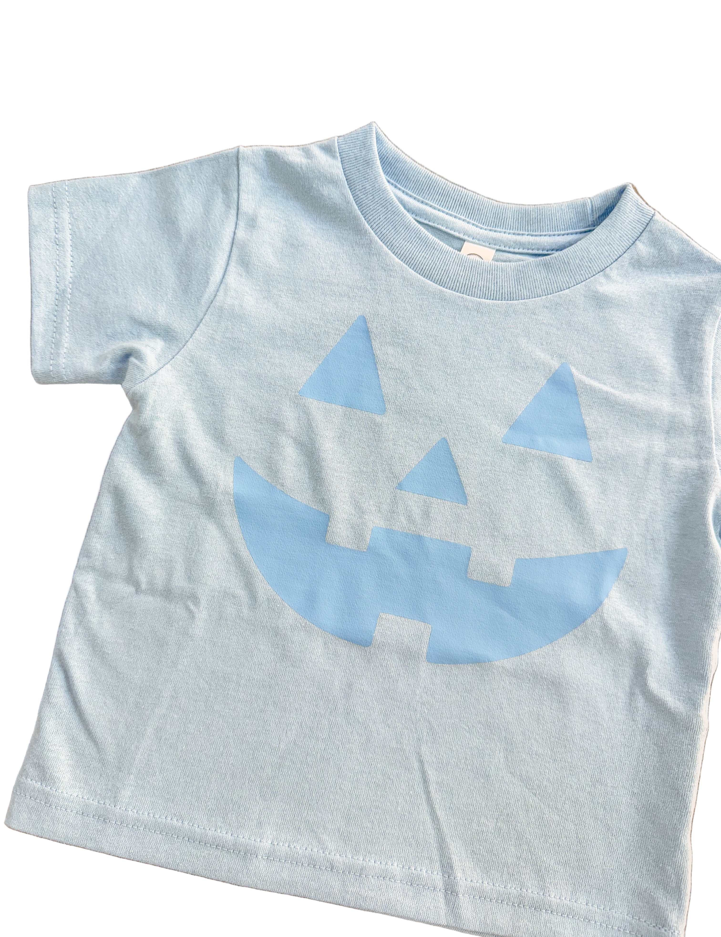 Light blue t-shirt with a jack-o'-lantern face design on a wooden surface