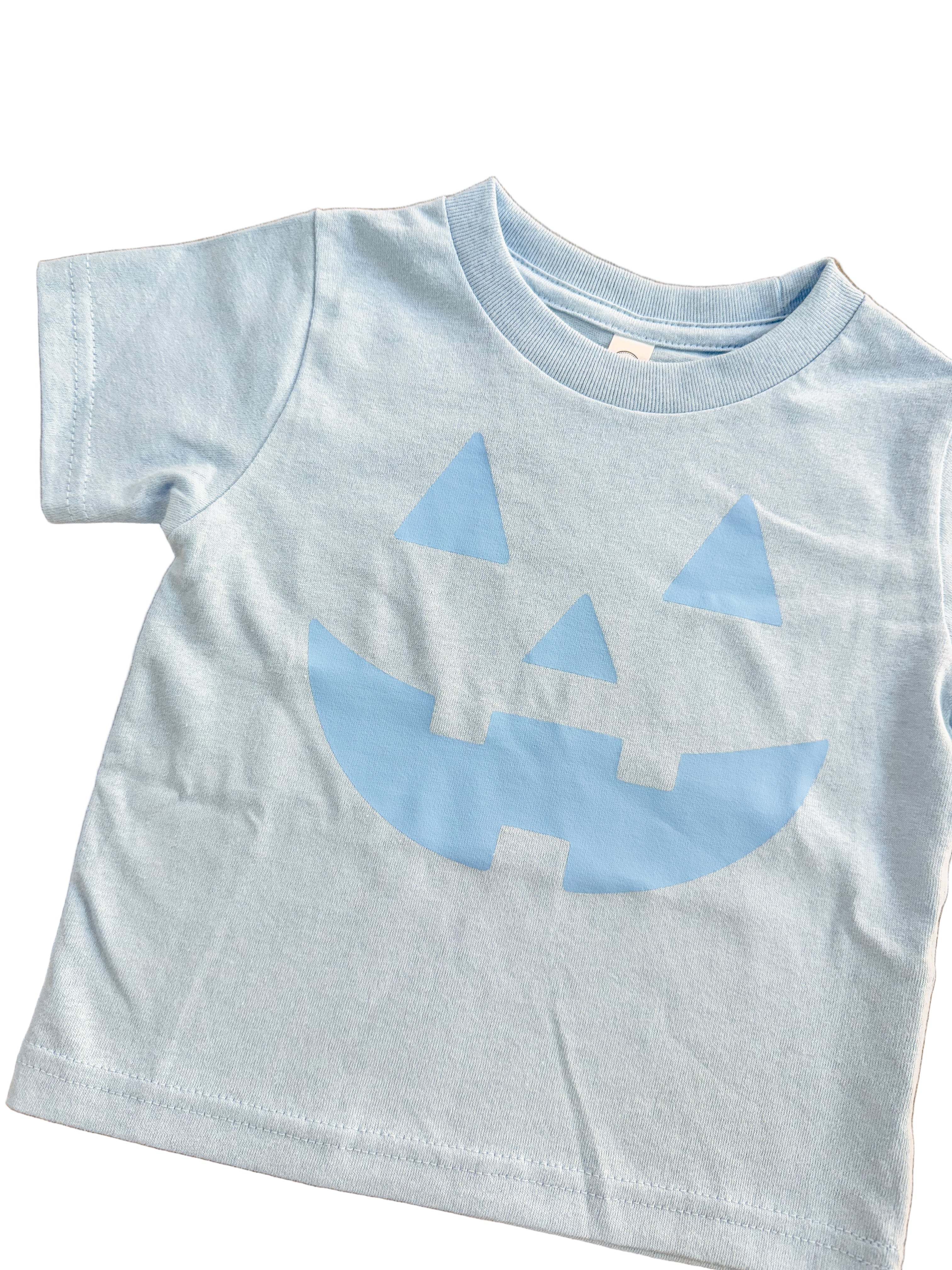 Light blue t-shirt with a jack-o'-lantern face design on a wooden surface