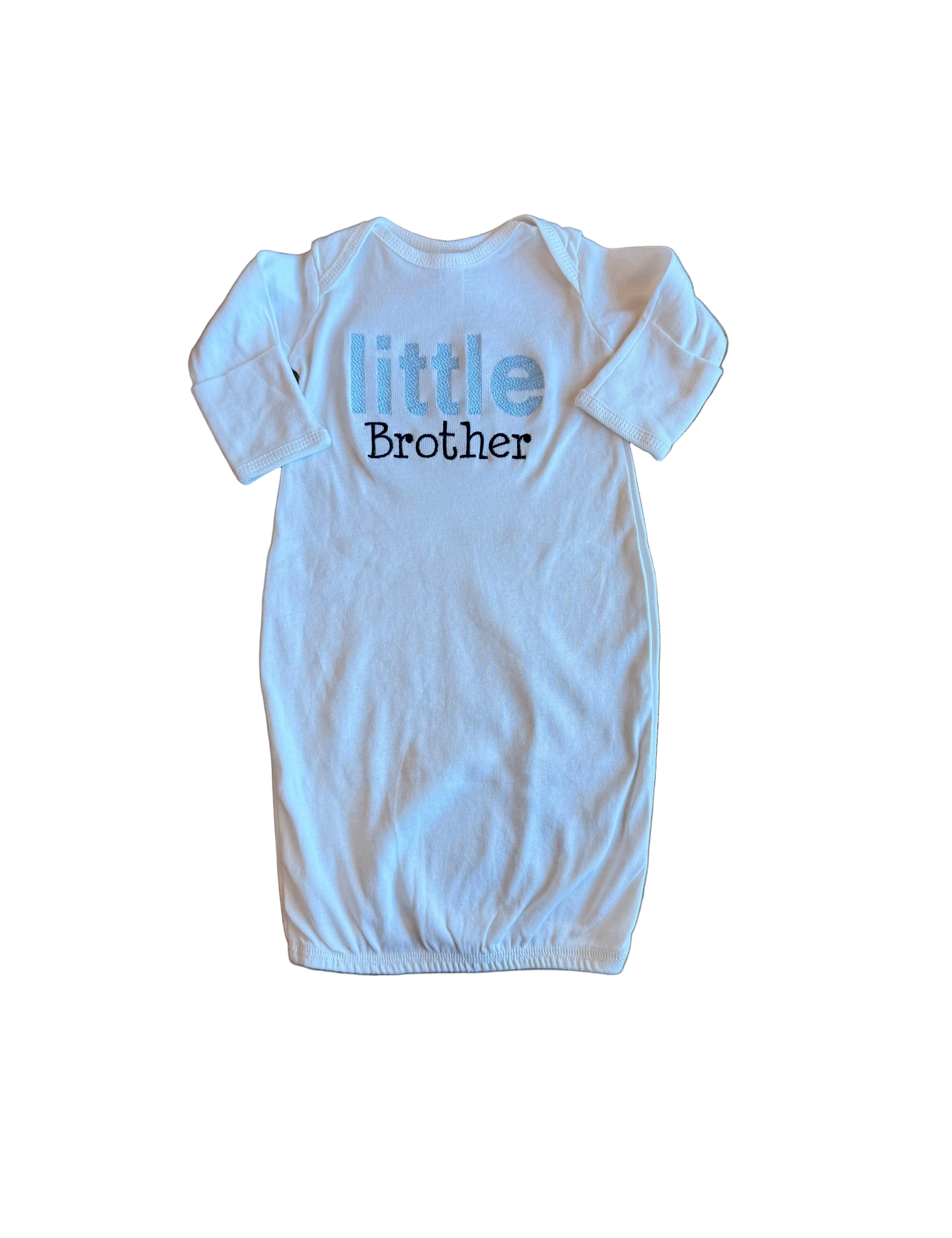 White baby onesie with 'little brother' text on a wooden floor