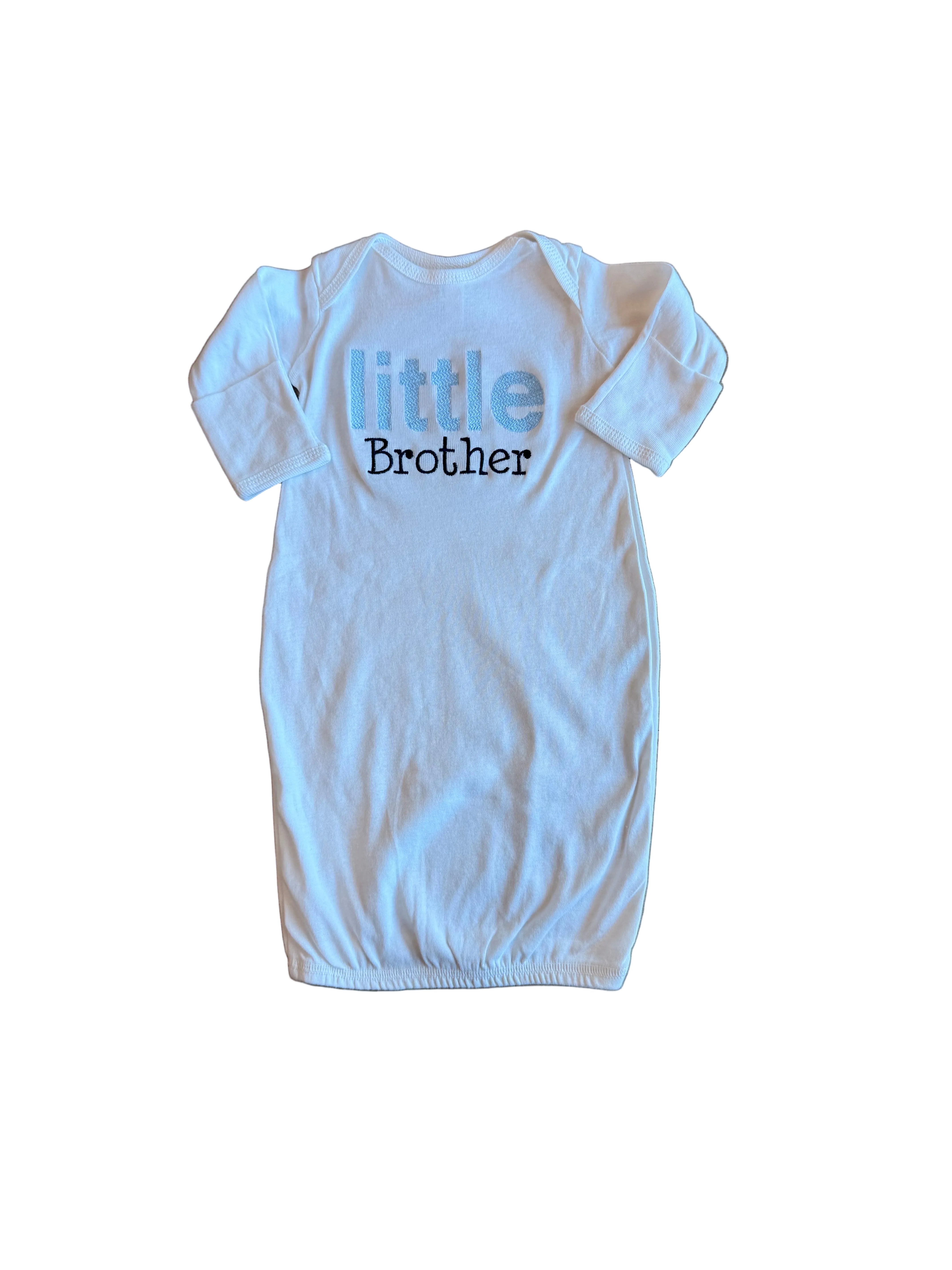 White baby onesie with 'little brother' text on a wooden floor