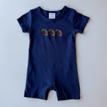 A navy blue baby romper with three embroidered footballs on the chest, laid flat against a light gray background.