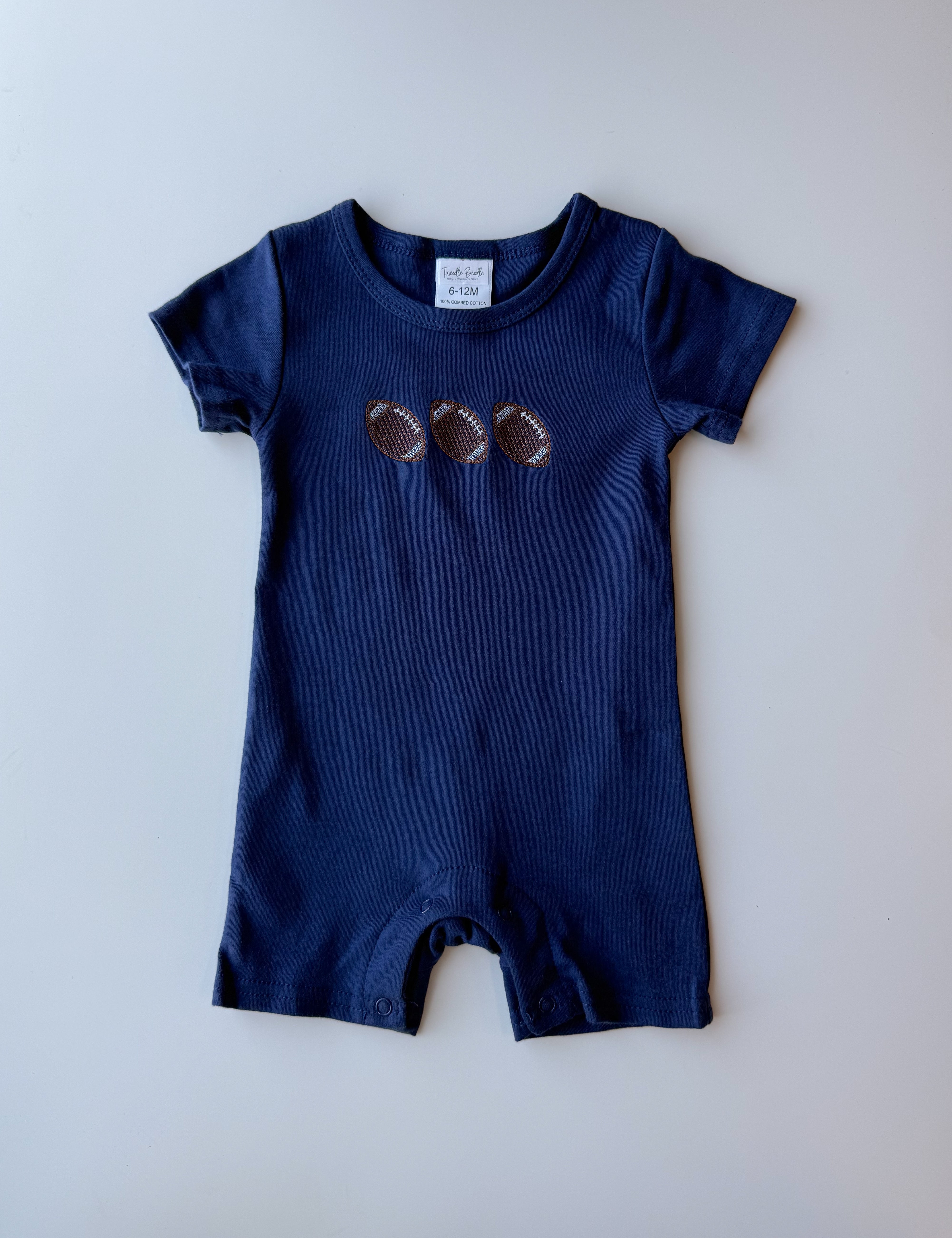 A navy blue baby romper with three embroidered footballs on the chest, laid flat against a light gray background.