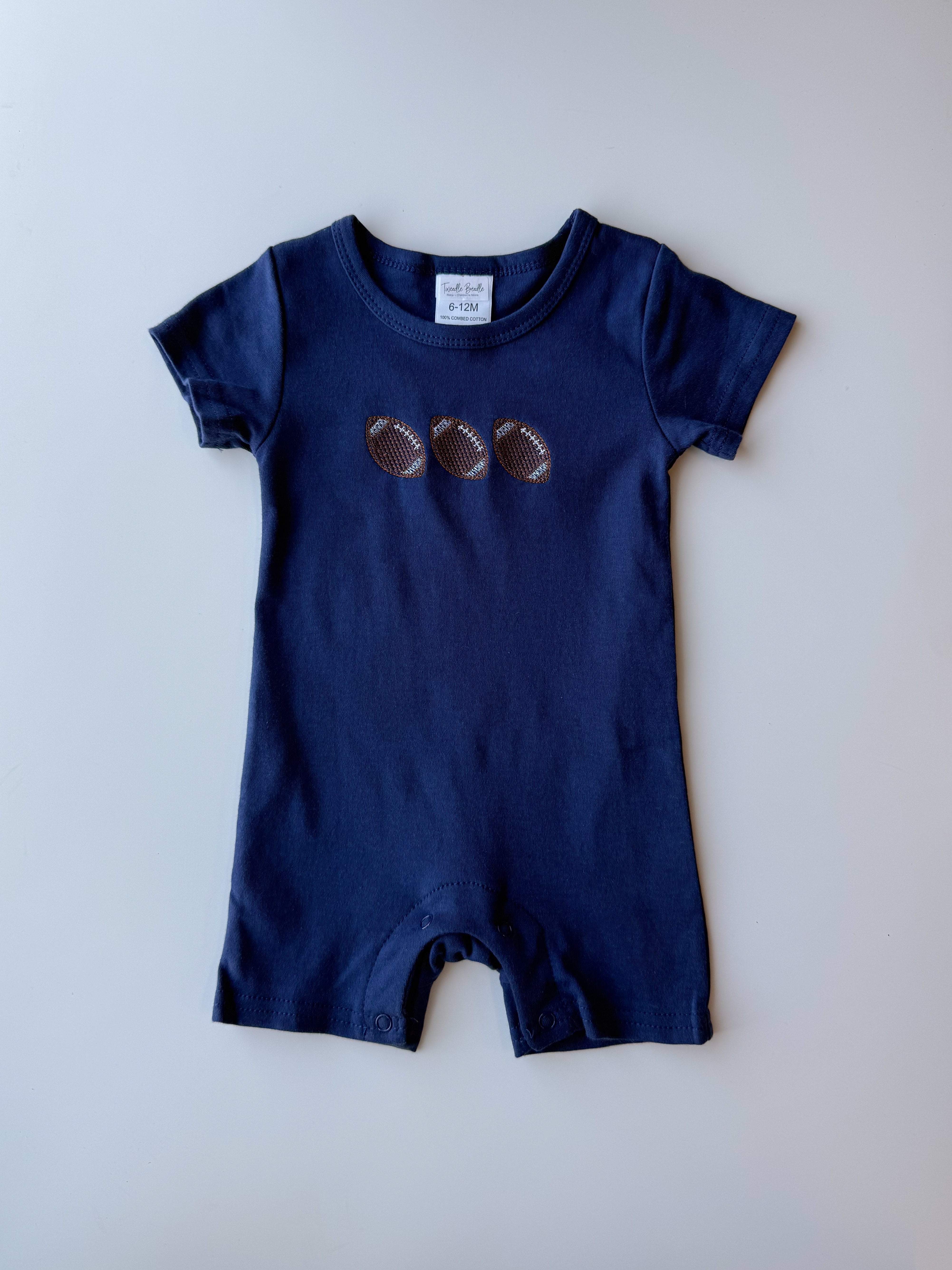 A navy blue baby romper with three embroidered footballs on the chest, laid flat against a light gray background.